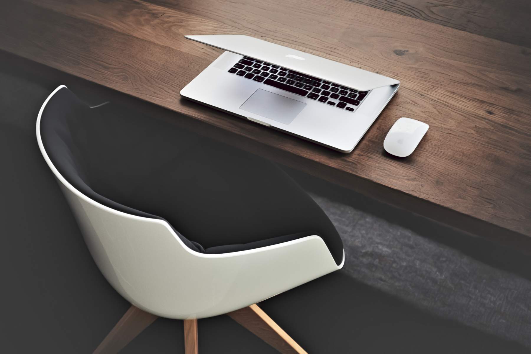 une chaise blanche et noire façon vintage disposée devant un bureau en bois supportant une souris blanche et un ordinateur portable dont le capot est fermé aux deux tiers.
